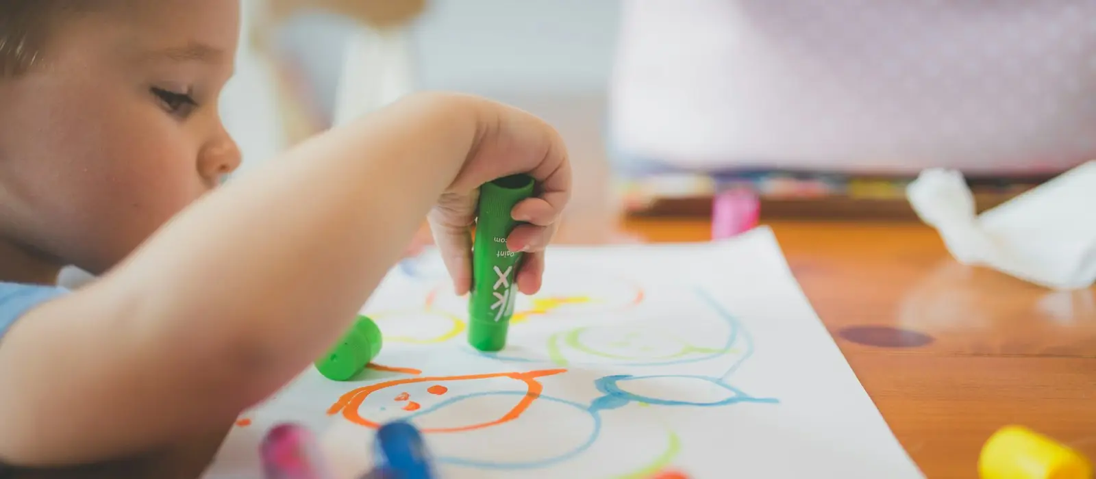 A toddler holding a green crayon and drawing colorful scribbles on paper