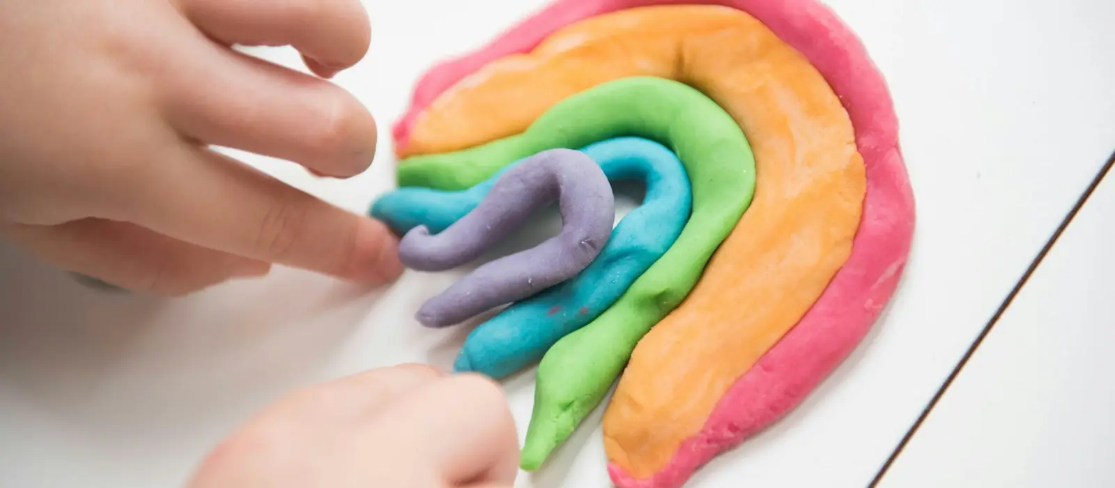 Small hands shaping a rainbow out of colorful homemade playdough