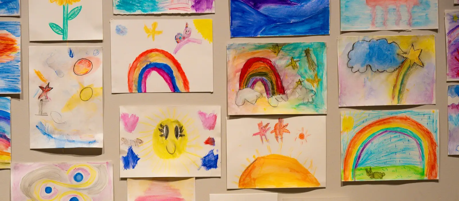 A wall covered with children's colorful paintings of rainbows, flowers and suns