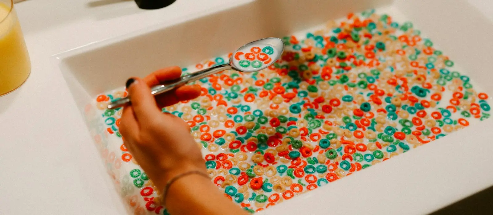 A child's hand scooping colorful cereal from a white tub with a spoon